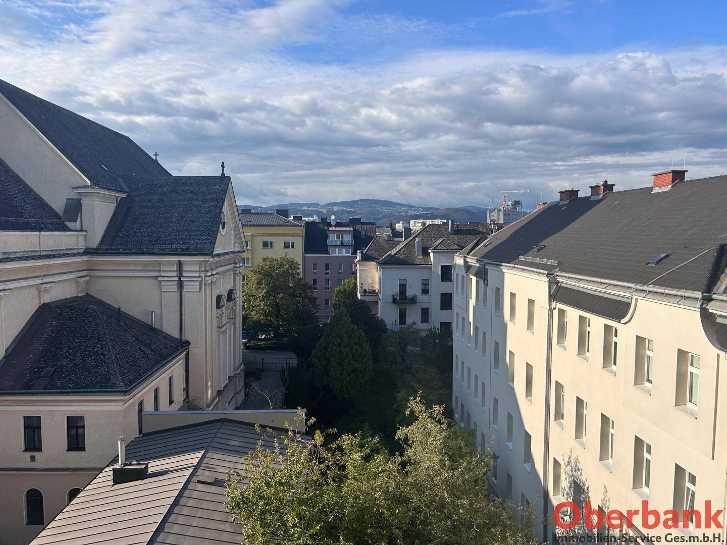 Blick über die Dächer der Stadt mit historischen Gebäuden und Bergen im Hintergrund.
