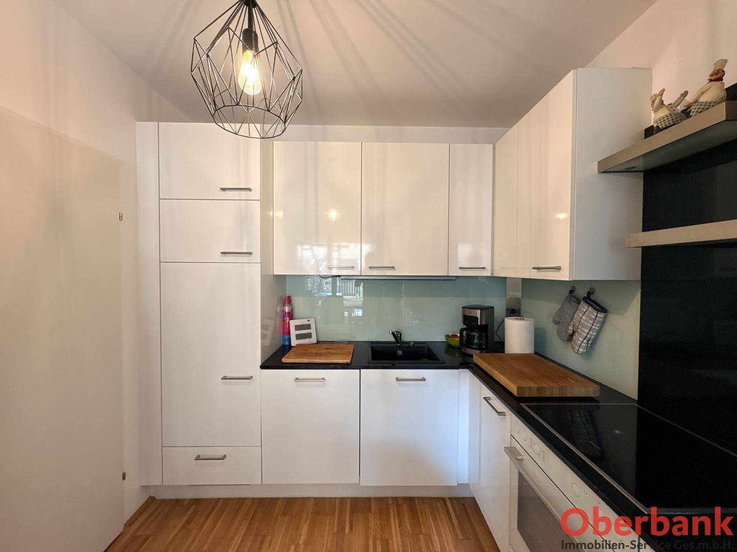 Moderne Einbauküche mit weißen Hochglanzfronten, dunkler Arbeitsplatte und Holzfußboden.