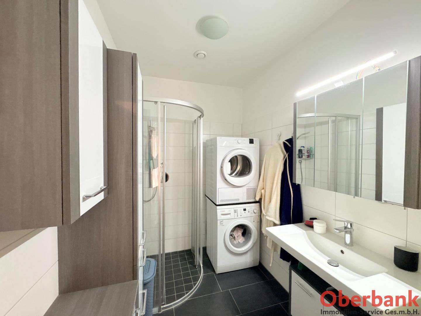 Modernes Badezimmer mit Dusche, Waschbecken und gestapelter Waschmaschine und Trockner.