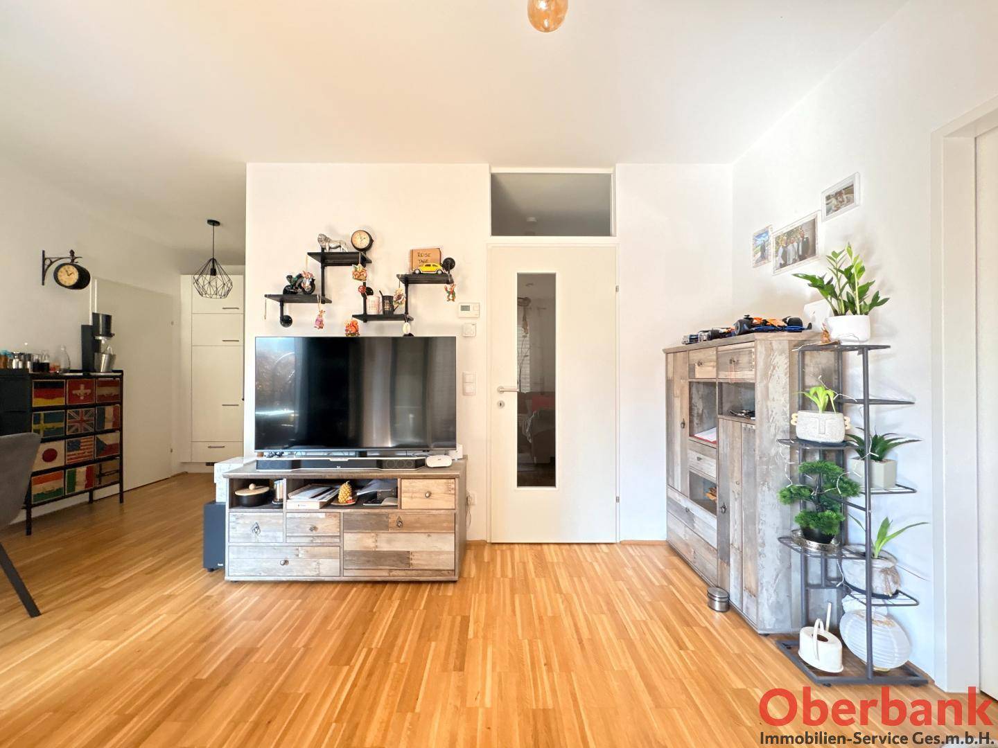 Geräumiger Wohnbereich mit hellem Holzfußboden, weiß gestrichenen Wänden und modernen Möbeln.