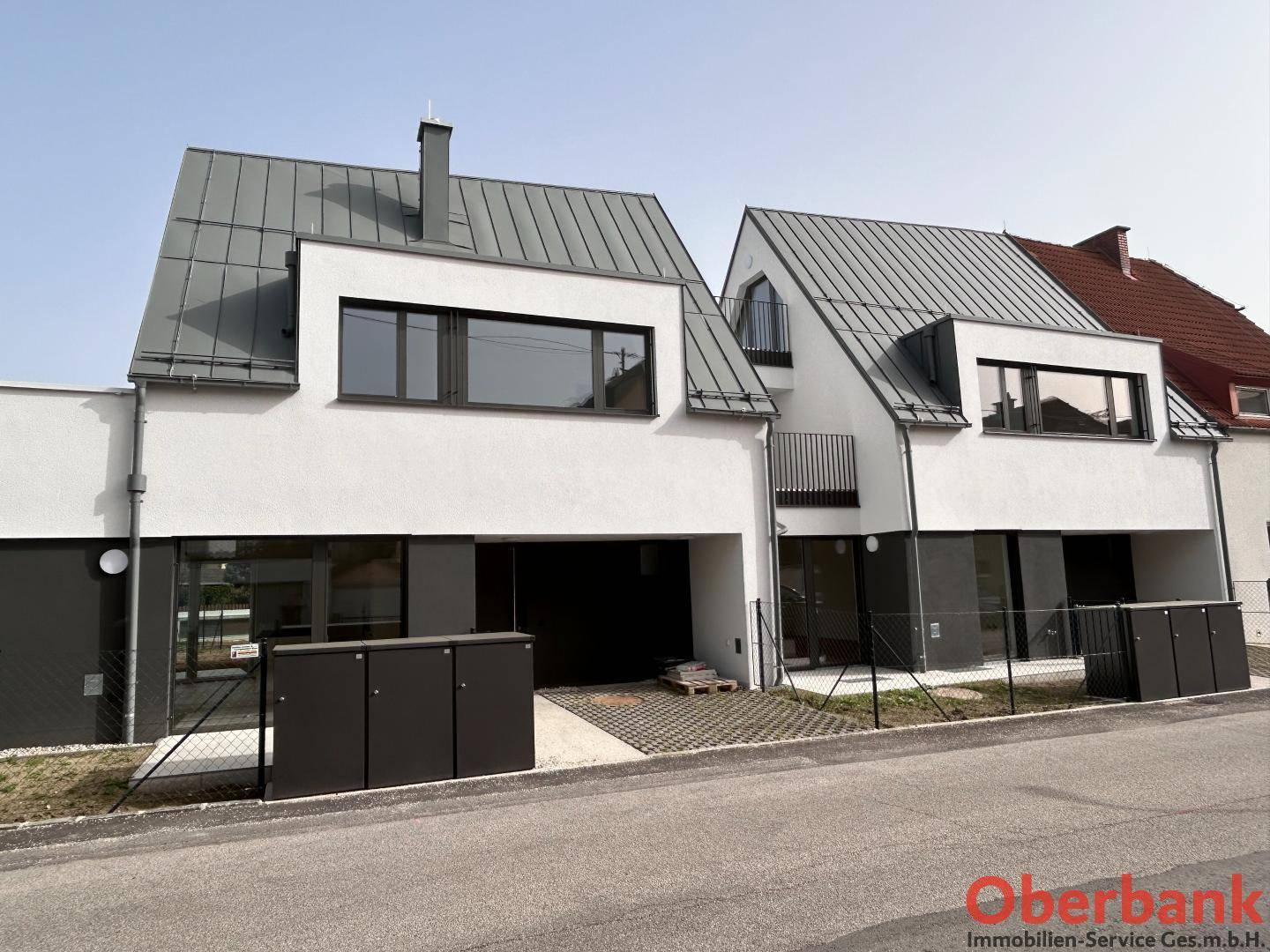 Zwei moderne Doppelhaushälften mit weißer Fassade und grauen Dächern in einer Wohnsiedlung.
