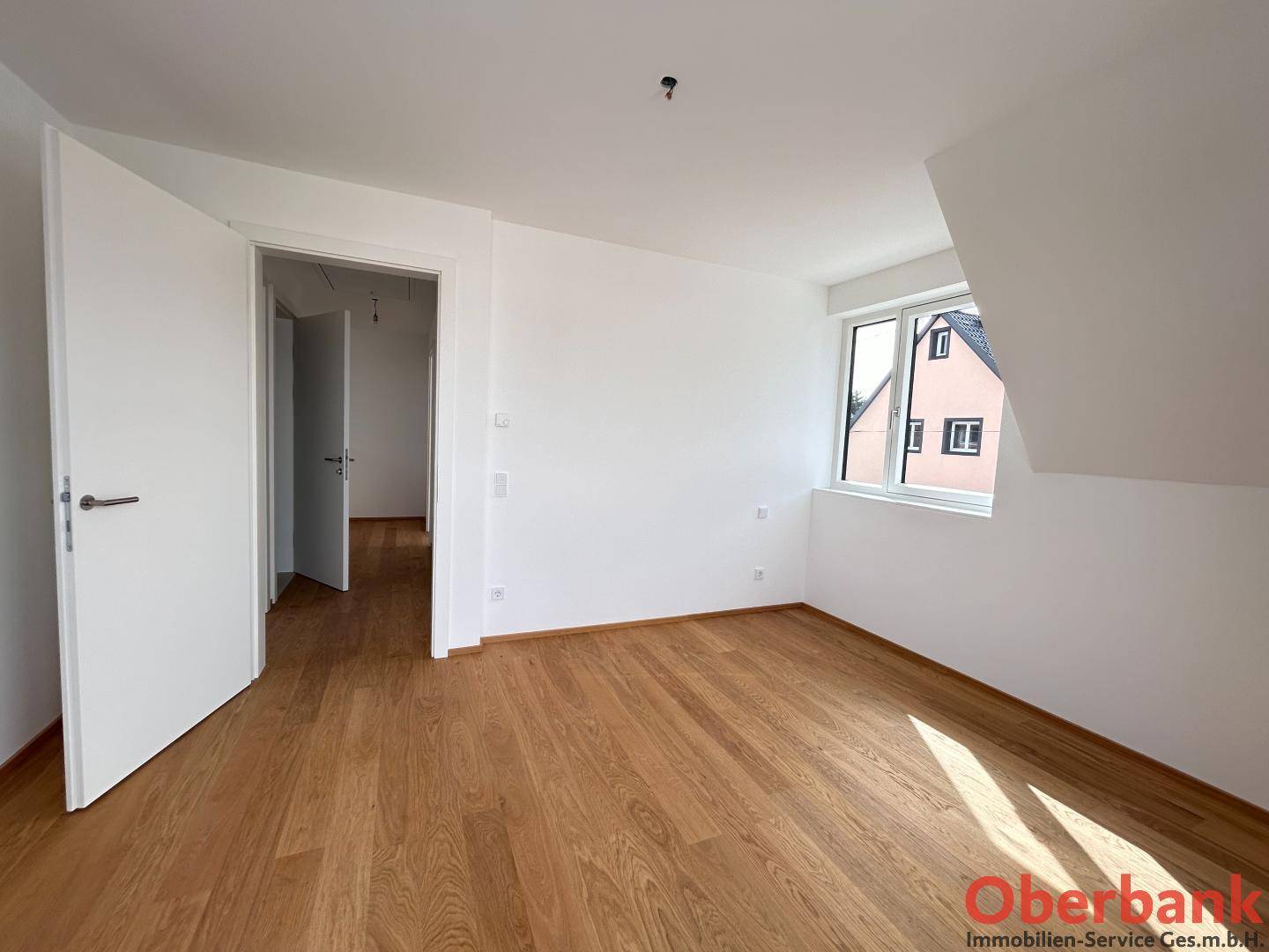 Leeres Schlafzimmer mit Holzboden, weißen Wänden und einer Tür zu einem weiteren Raum.