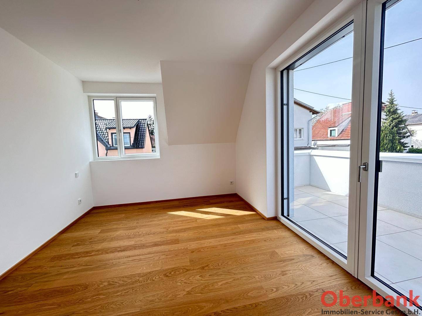Helles Schlafzimmer mit Holzboden, Dachschräge und Zugang zu einem Balkon.