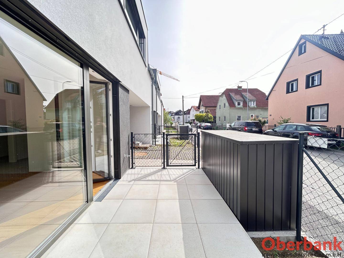 Helle Terrasse mit Fliesenboden und Zugang zum Innenbereich, umgeben von einem Zaun.