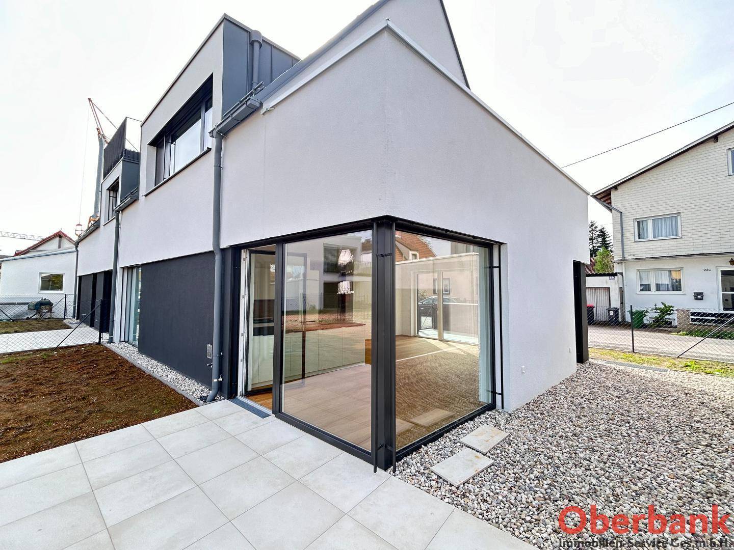 Seitliche Ansicht des Hauses mit großer Glasfront, Terrasse und Kiesbereich im Garten.