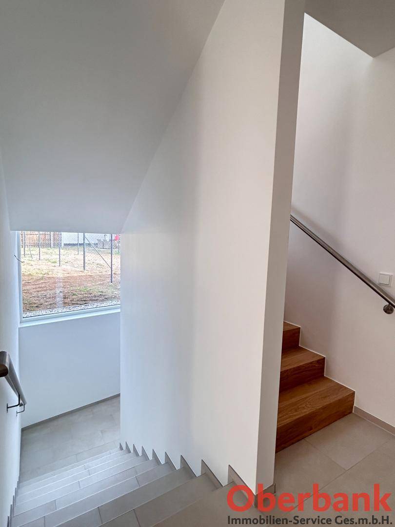 Moderner Treppenbereich mit Holzstufen, Fliesenboden und einem Fenster im unteren Bereich.