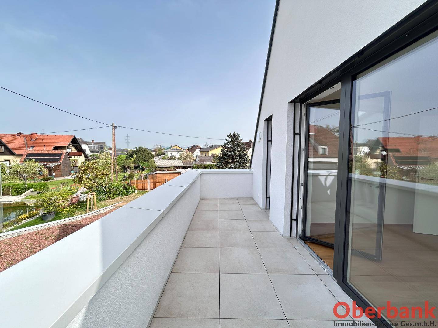 Langer Balkon mit Fliesenboden und Blick auf die umliegende Wohngegend und Grünflächen.