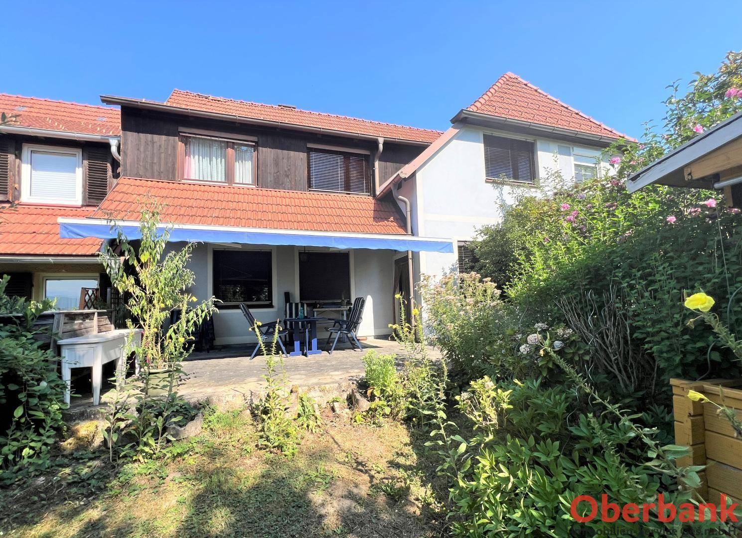 Sonniger Terrassenbereich mit blauer Markise und Gartenmöbeln, ideal für entspannte Stunden im Freien.