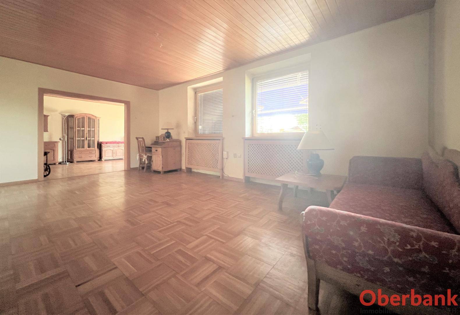 Geräumiges Wohnzimmer mit Fischgrätparkett und Holzdecke, bietet viel Platz für individuelle Gestaltung.
