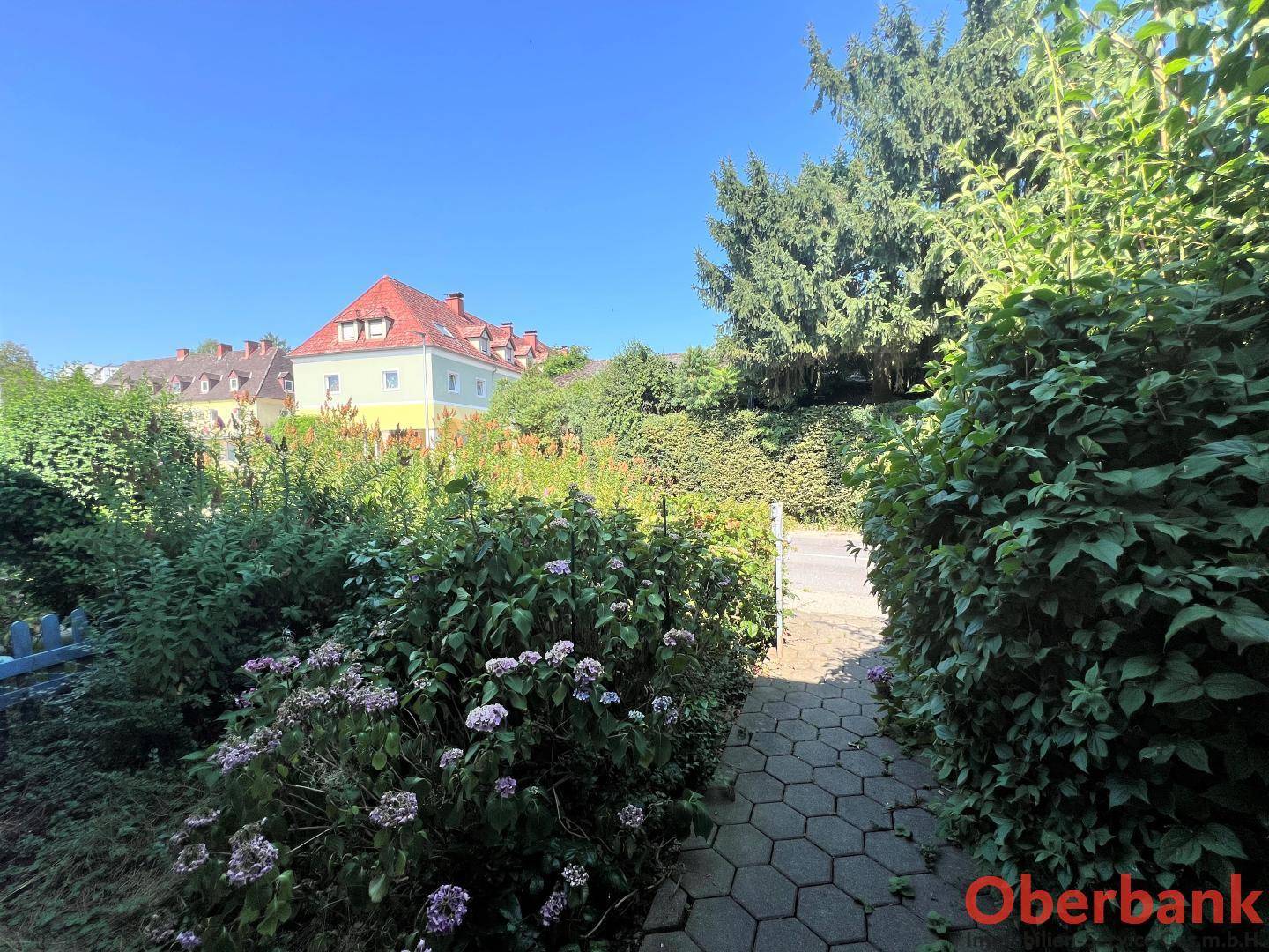 Gepflasterter Gartenweg führt durch blühende Beete mit Blick auf die umliegende Nachbarschaft.