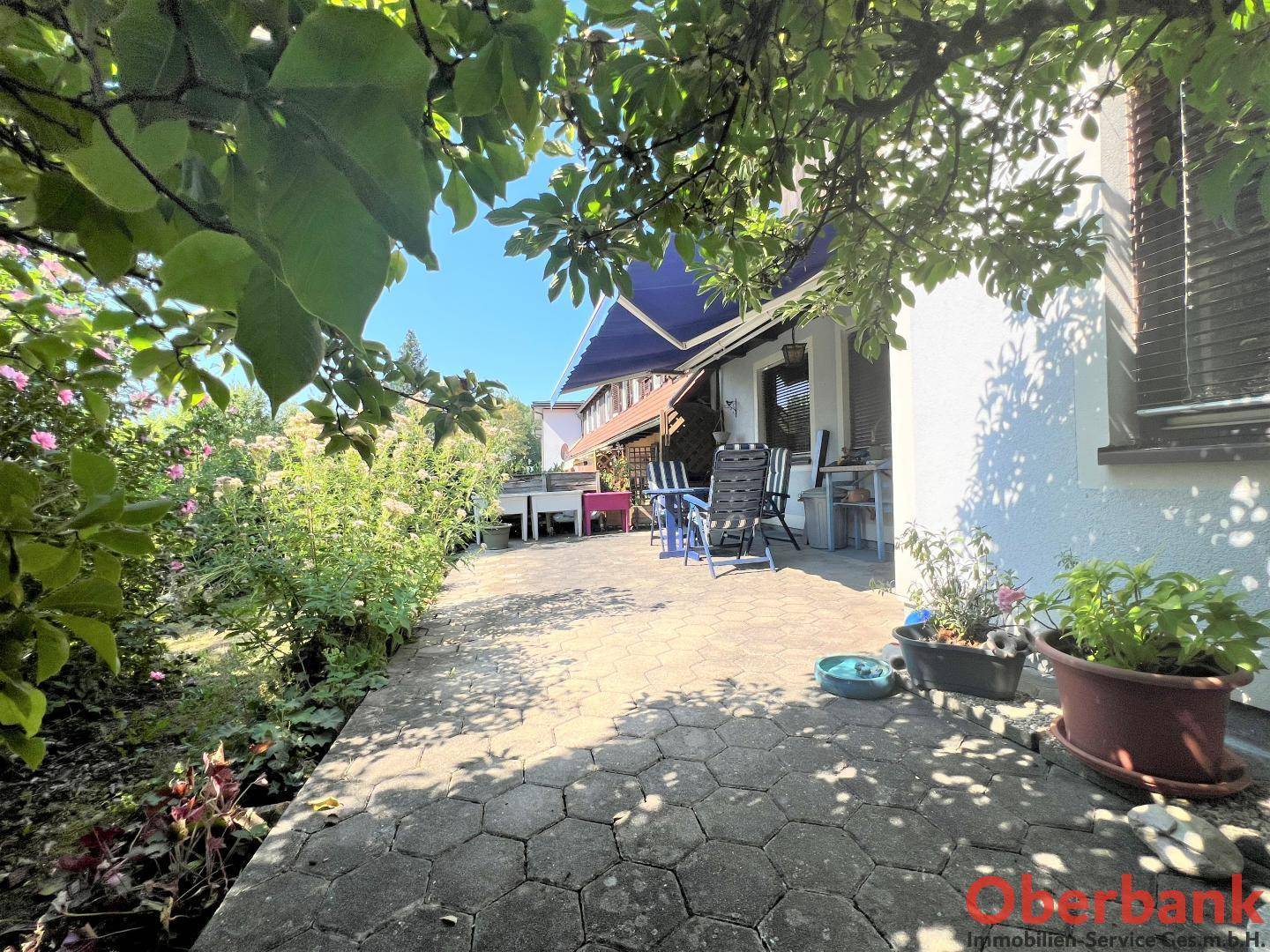 Große gepflasterte Terrasse mit Zugang zum Garten, umgeben von blühenden Sträuchern.