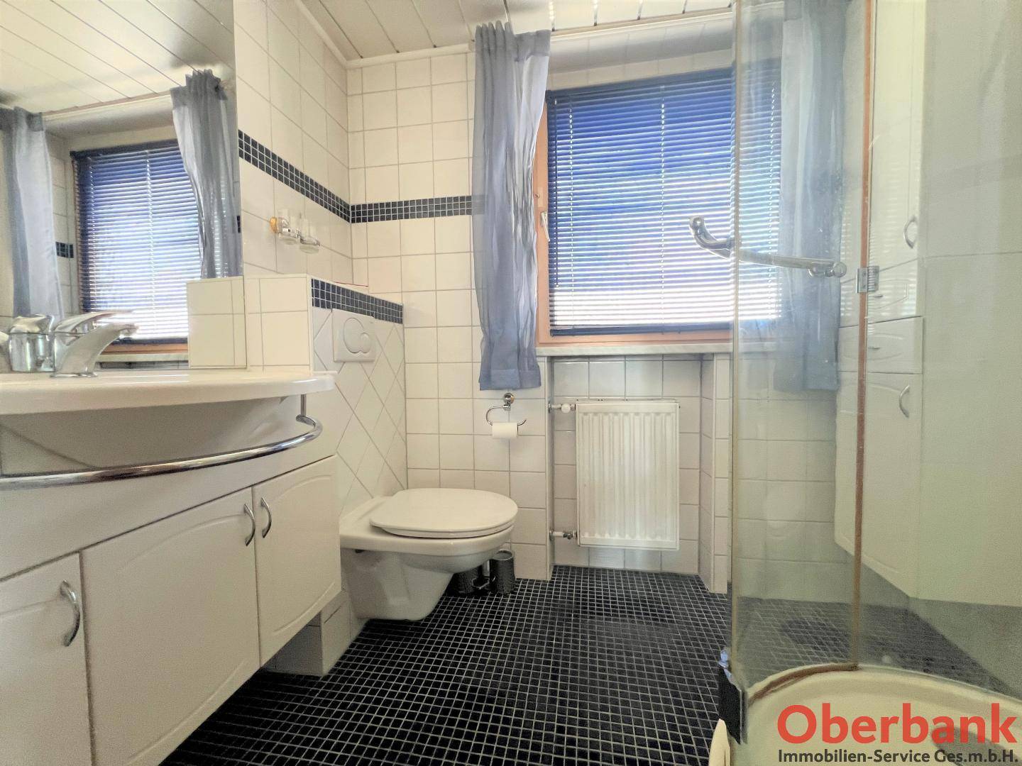 Badezimmer mit Dusche, WC und Waschbecken, ausgestattet mit weißen Fliesen und Fenster.