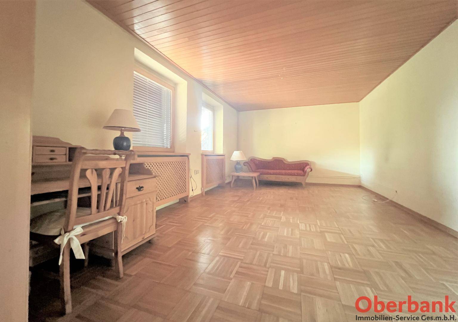 Wohnzimmer mit Parkettboden und Holzdecke, bietet eine gemütliche Atmosphäre mit viel Tageslicht.