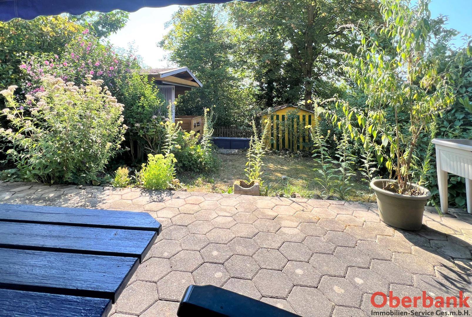 Blick von der Terrasse in den gepflegten Garten mit Gartenhäuschen und viel Grün.