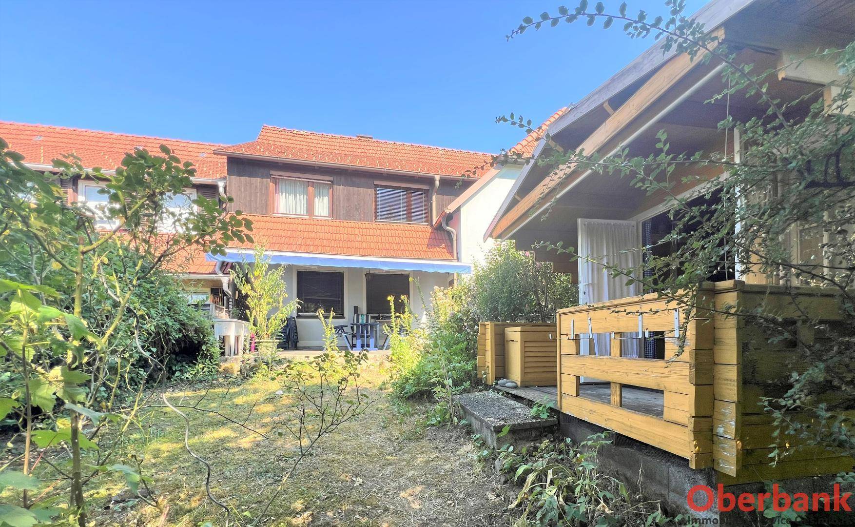 Blick auf die hintere Hausfassade mit Terrasse und Garten, umgeben von viel Grün.