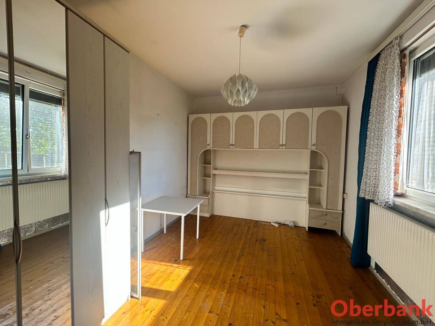 Helles Schlafzimmer mit Holzboden, Einbauschränken und großen Fenstern für viel Tageslicht.