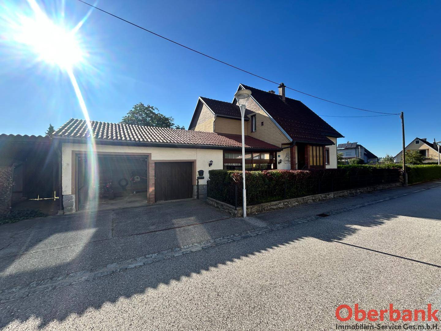 Ansicht des Hauses von der Straße mit Doppelgarage und gepflegter Hecke unter blauem Himmel.