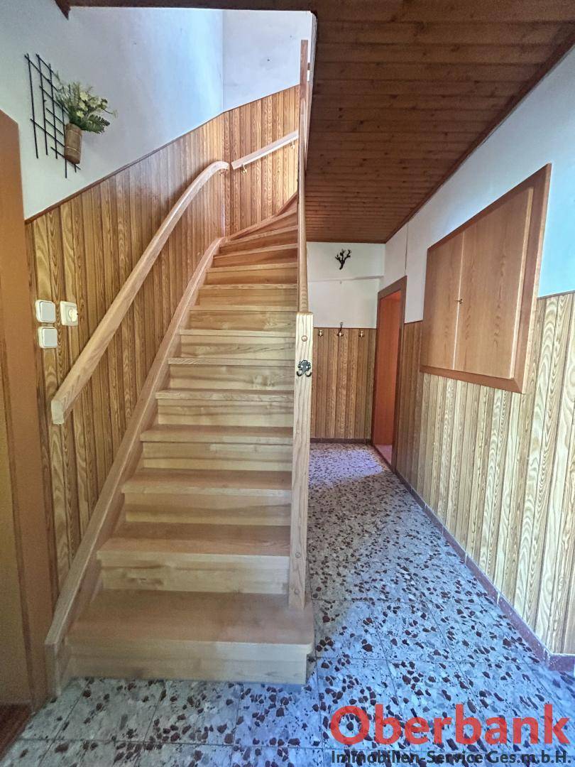 Heller Flur mit Holztreppe, Holzvertäfelung und gemustertem Fliesenboden im Eingangsbereich.