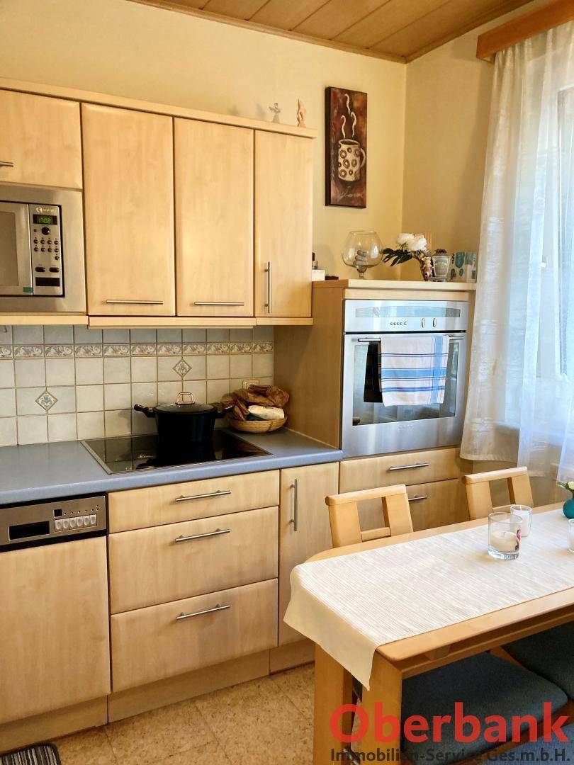 Helle Einbauküche mit Holzfronten, modernen Geräten und einem kleinen Essbereich.