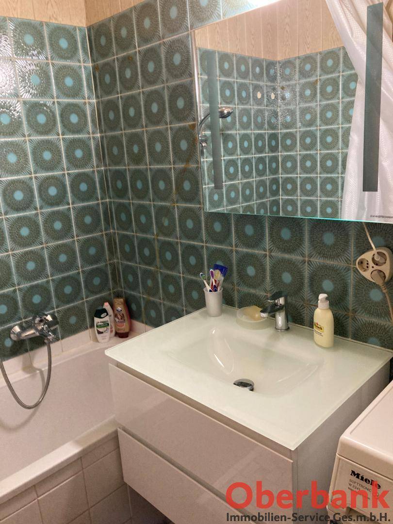 Badezimmer mit Badewanne, modernem Waschbecken und auffälligen grünen Fliesen.