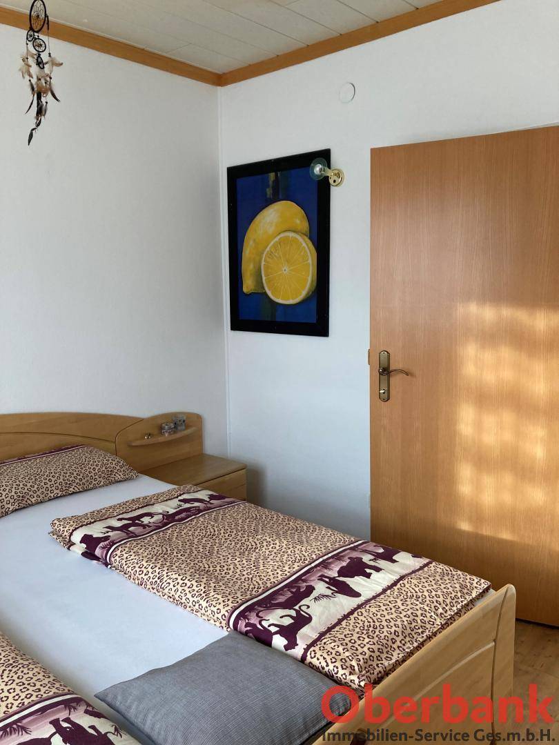Schlafzimmer mit Einzelbett, Nachttisch und Holztür, dekoriert mit Kunst.