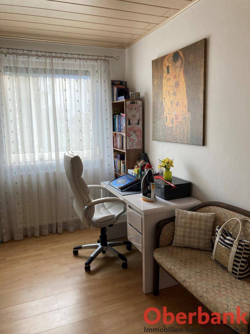 Helles Arbeitszimmer mit Schreibtisch, Bürostuhl und einem Sofa am Fenster.
