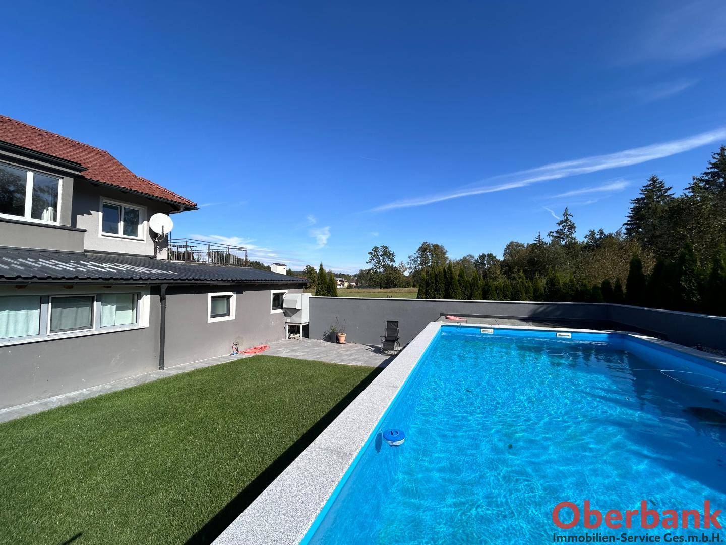 Weitläufiger Gartenbereich mit Schwimmbecken und Blick ins Grüne unter blauem Himmel.