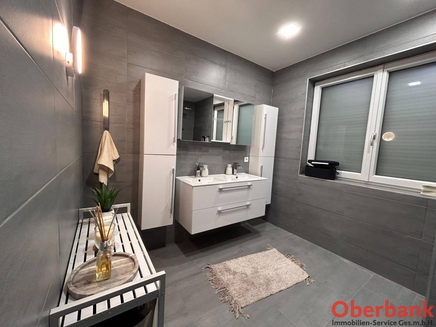 Modernes Badezimmer mit Doppelwaschbecken, Spiegelschrank und Fenster für Tageslicht.