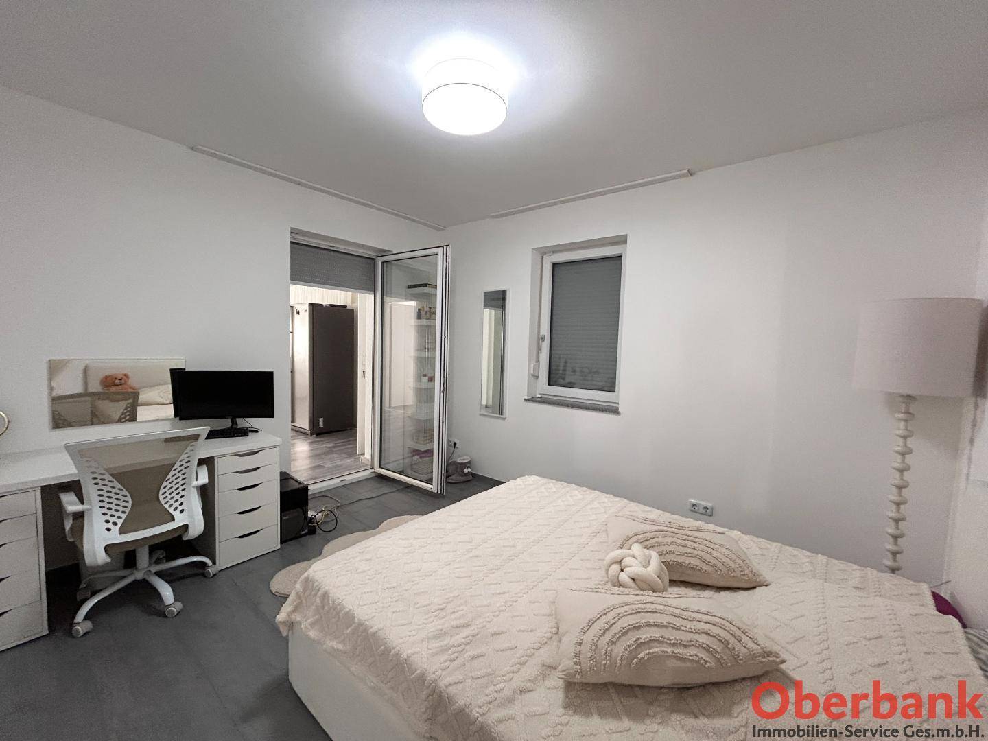 Schlafzimmer mit Doppelbett, Schreibtisch und Zugang zu einem weiteren Raum.