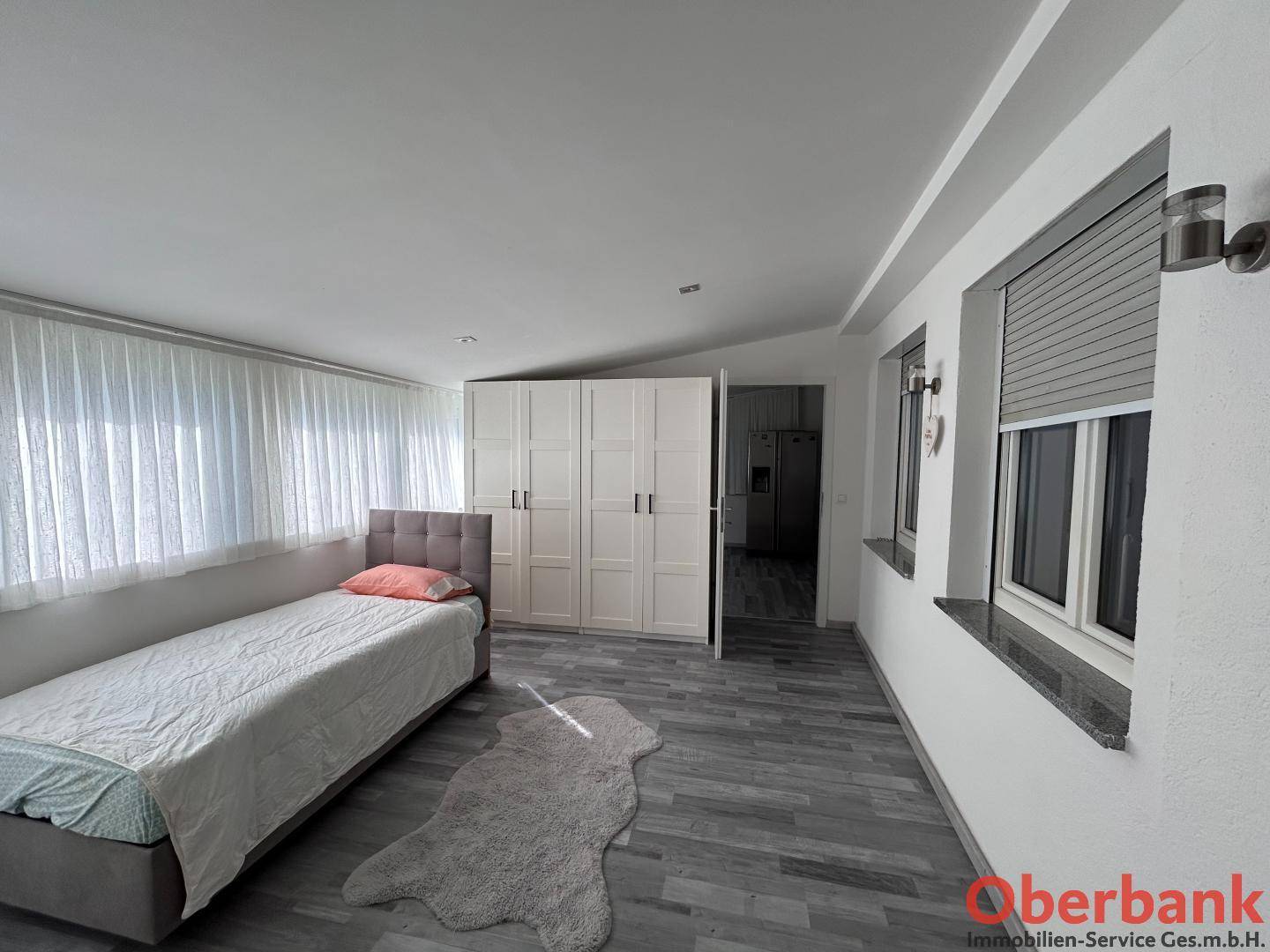 Helles Schlafzimmer mit Einzelbett und großen Fenstern, ausgestattet mit Einbauschränken.