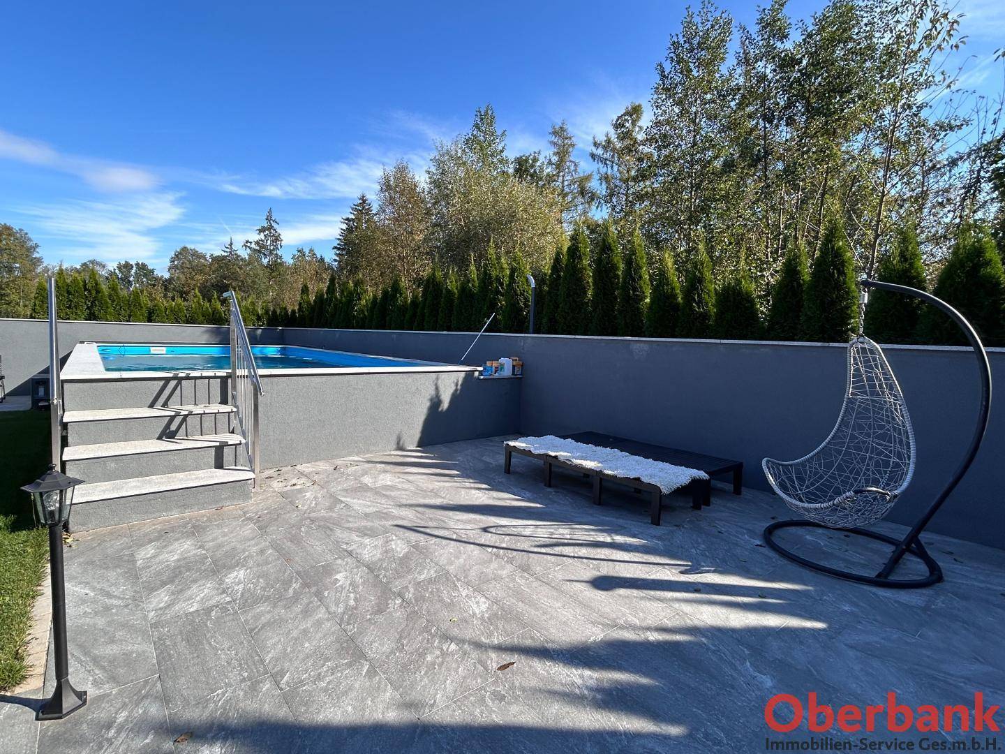 Entspannungsbereich am Pool mit Liegen und Hängesessel auf einer gefliesten Terrasse.
