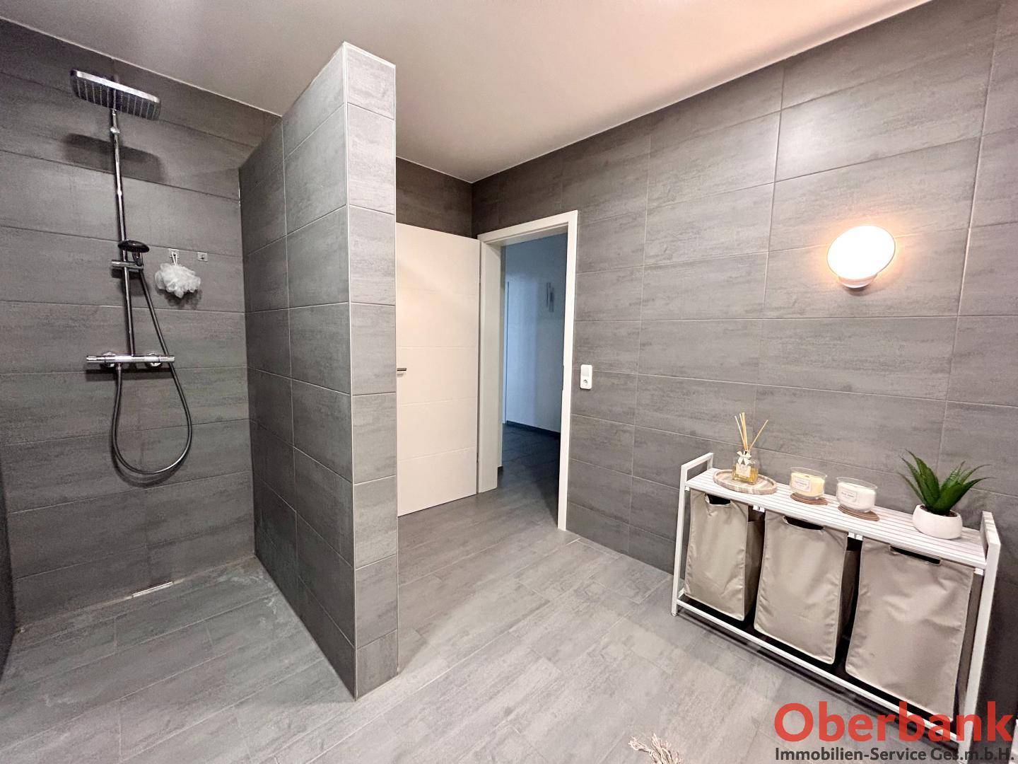 Modernes Badezimmer mit großer begehbarer Dusche und grauen Fliesen.