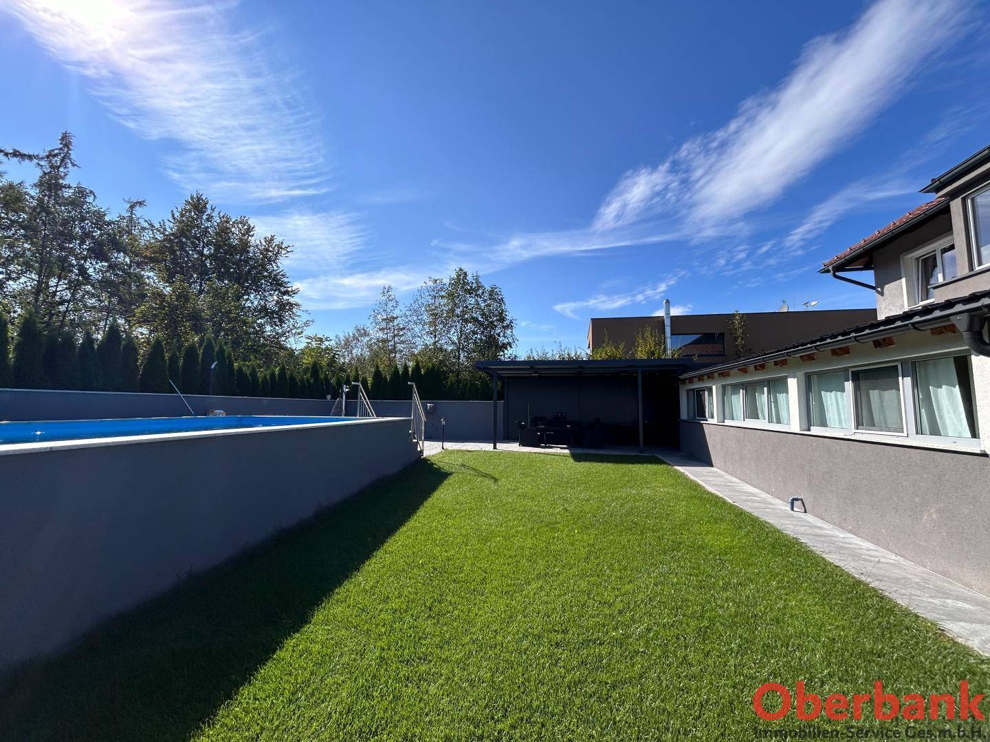 Sonniger Gartenbereich mit Rasen, Pool und überdachtem Außenbereich am Haus.