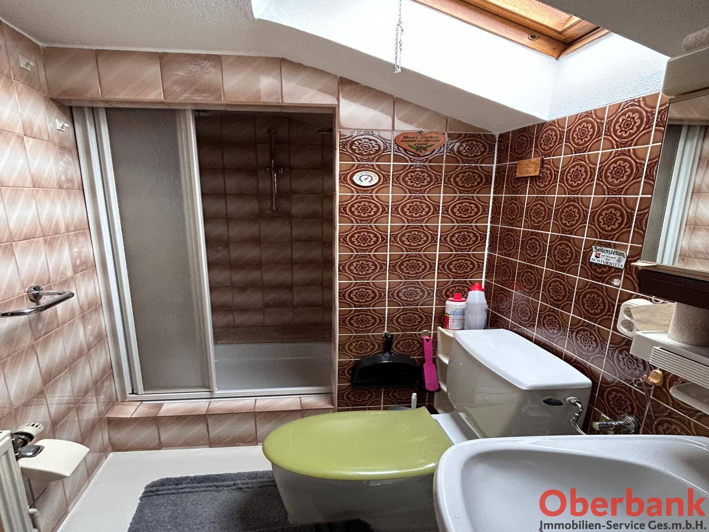 Badezimmer im 80er-Jahre-Stil mit Dusche, WC, Waschbecken und Dachfenster.