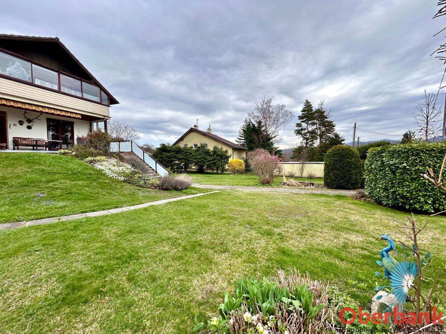 Garten mit Rasenfläche und blühenden Pflanzen, im Hintergrund das Haus und weitere Gebäude.