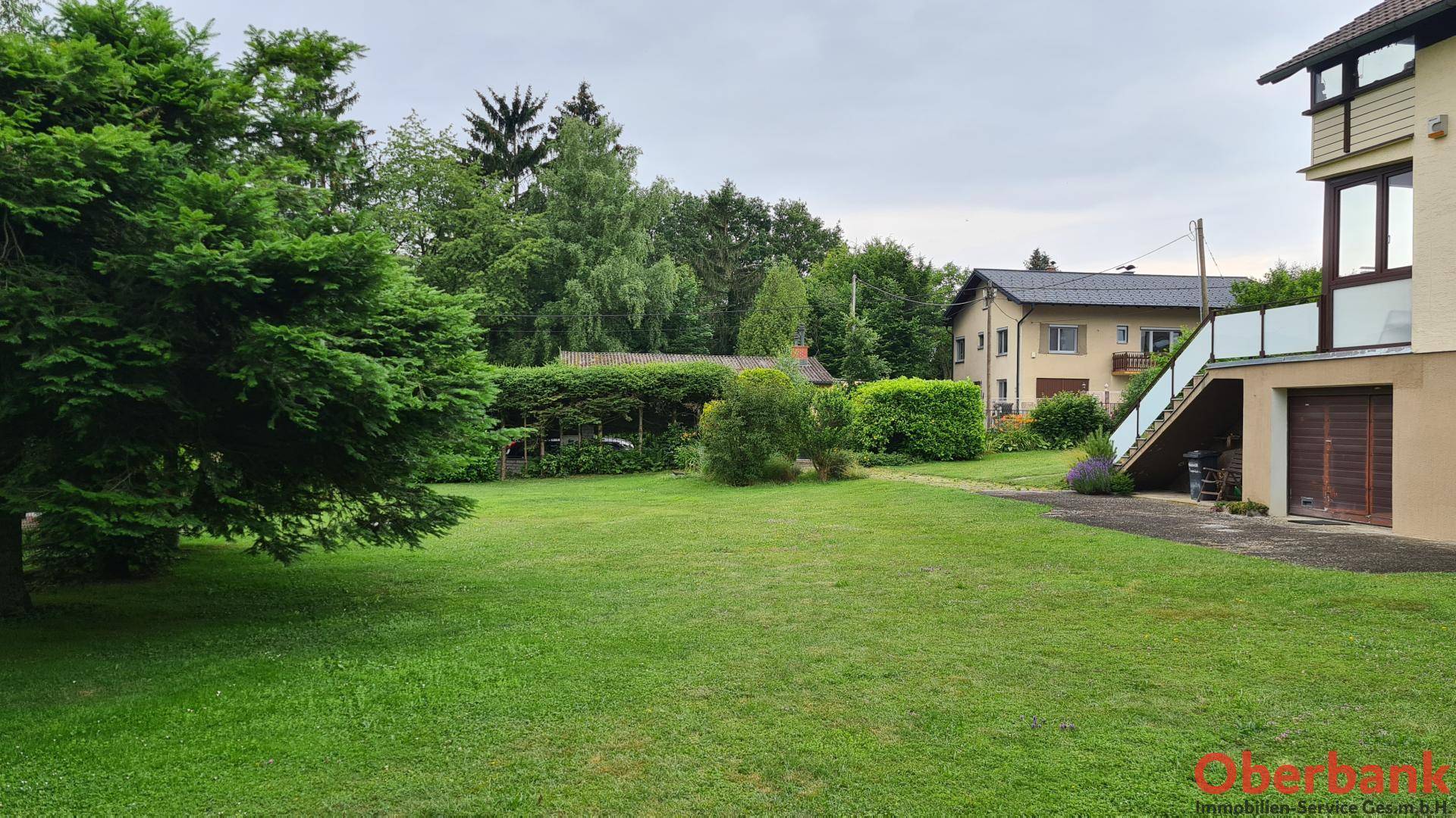 Weitläufiger Gartenbereich mit Rasen und Hecken, umgeben von Bäumen und Nachbarhäusern.