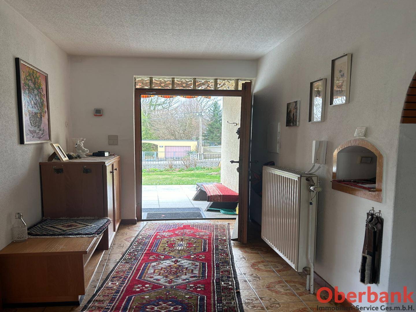 Heller Flur mit Fliesenboden, Teppich und Blick zum Hauseingang und Garten.