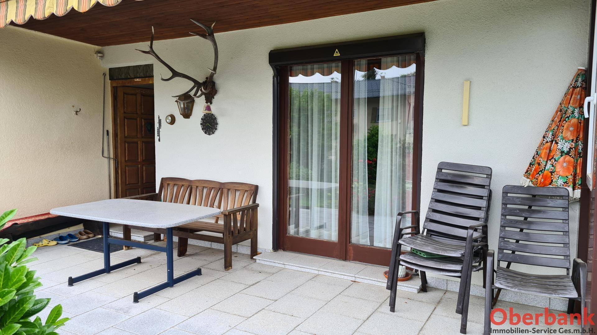Überdachte Terrasse mit Sitzgelegenheiten und traditioneller Hirschgeweih-Dekoration an der Wand.