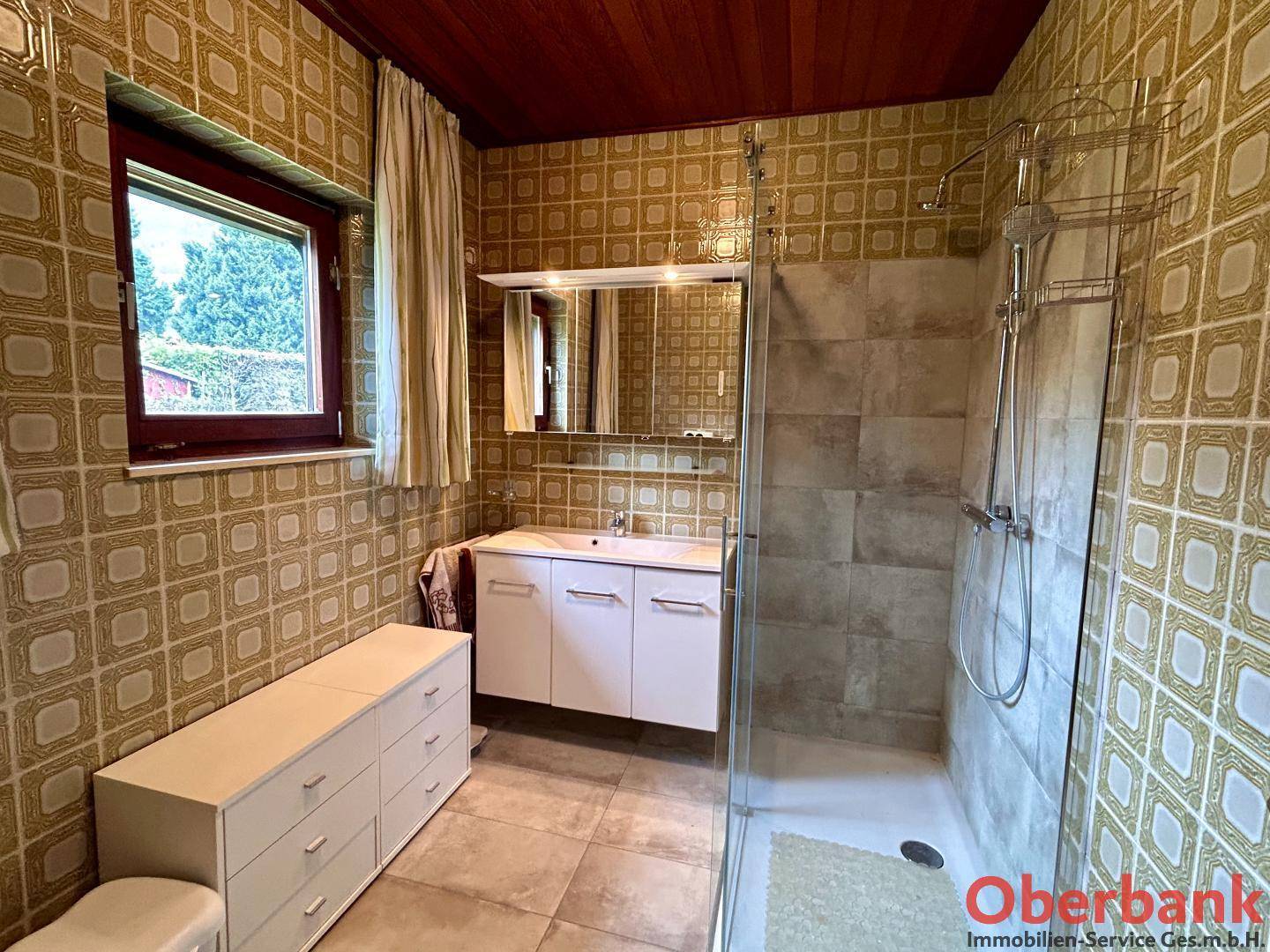 Modernisiertes Badezimmer mit begehbarer Dusche, Waschtisch und Fenster für Tageslicht.