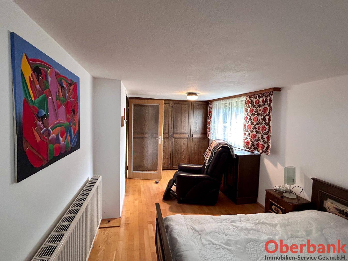 Schlafzimmer mit Holzboden, großem Gemälde und Einbauschrank in warmen Farbtönen.