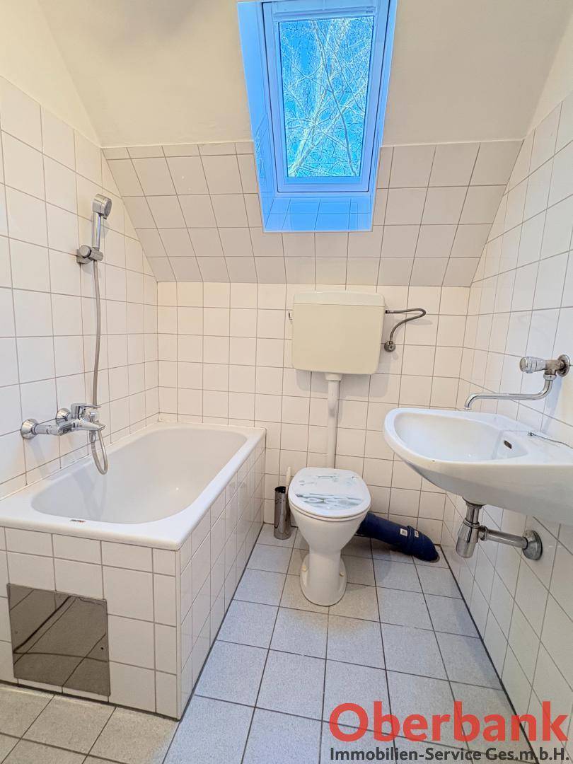 Gefliestes Badezimmer mit Badewanne, Toilette, Waschbecken und einem Dachfenster für Tageslicht.
