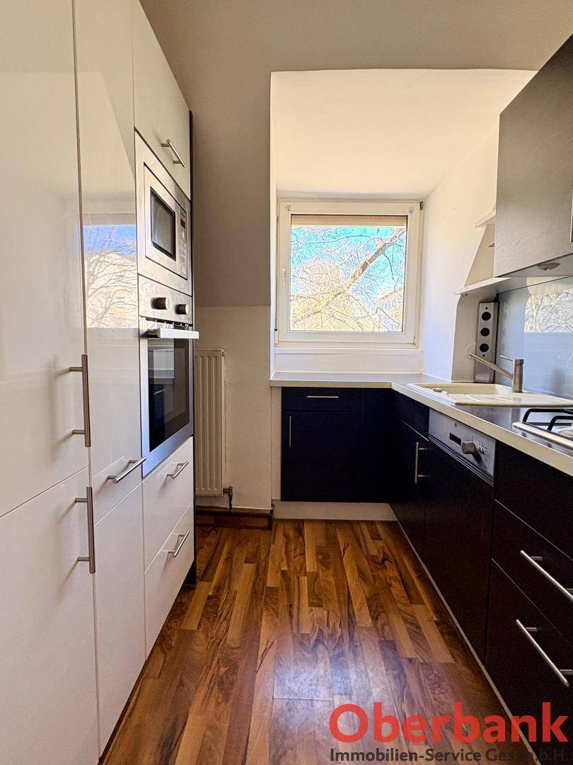 Moderne Küche mit weißen und dunklen Schränken, Einbaugeräten und Fenster unter der Dachschräge.