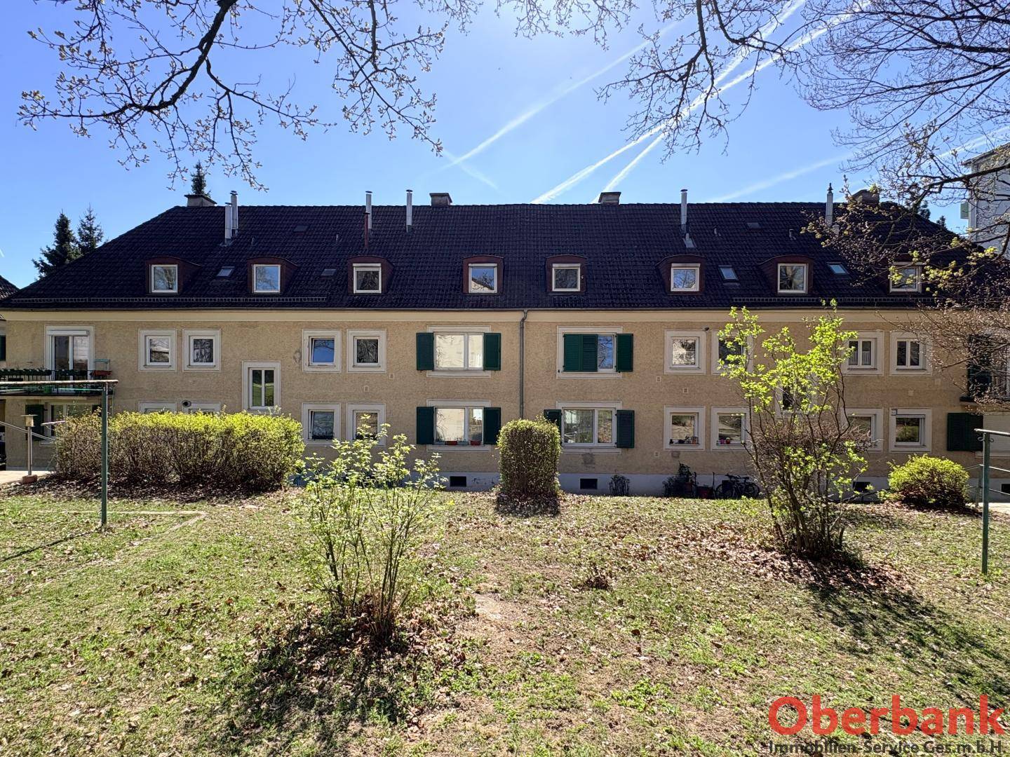 Mehrfamilienhaus mit gepflegter Fassade, Dachgauben und einem grünen Vorgarten.