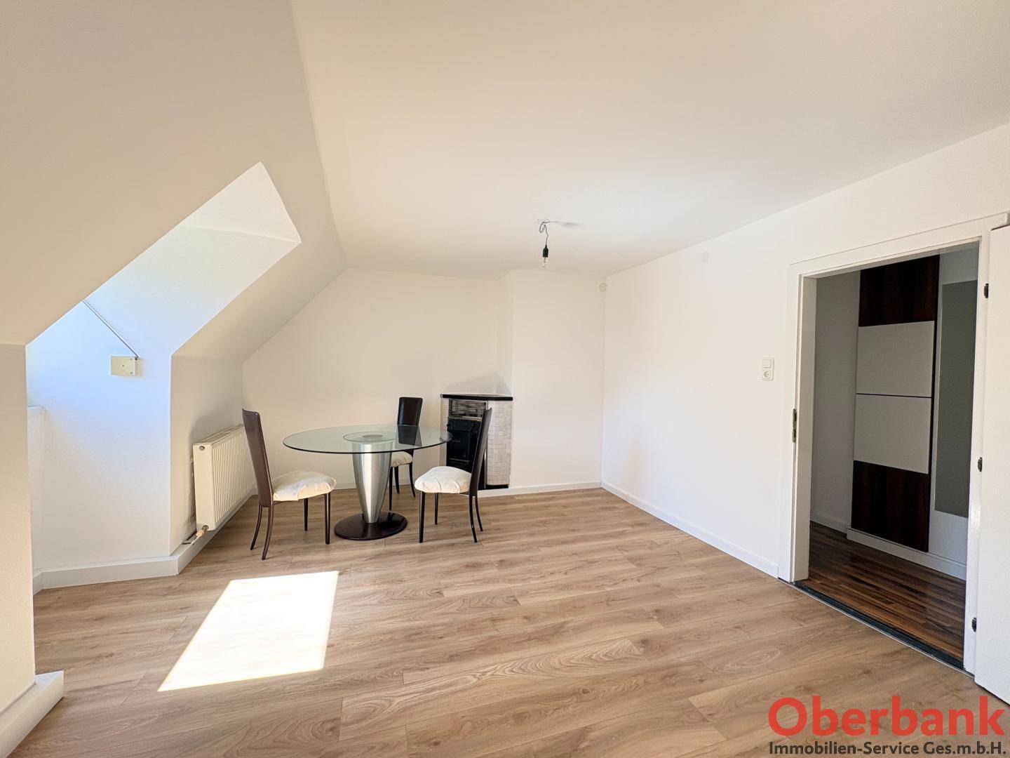 Geräumiger Wohnbereich mit Holzboden, Dachschrägen und Zugang zu einem weiteren Zimmer.
