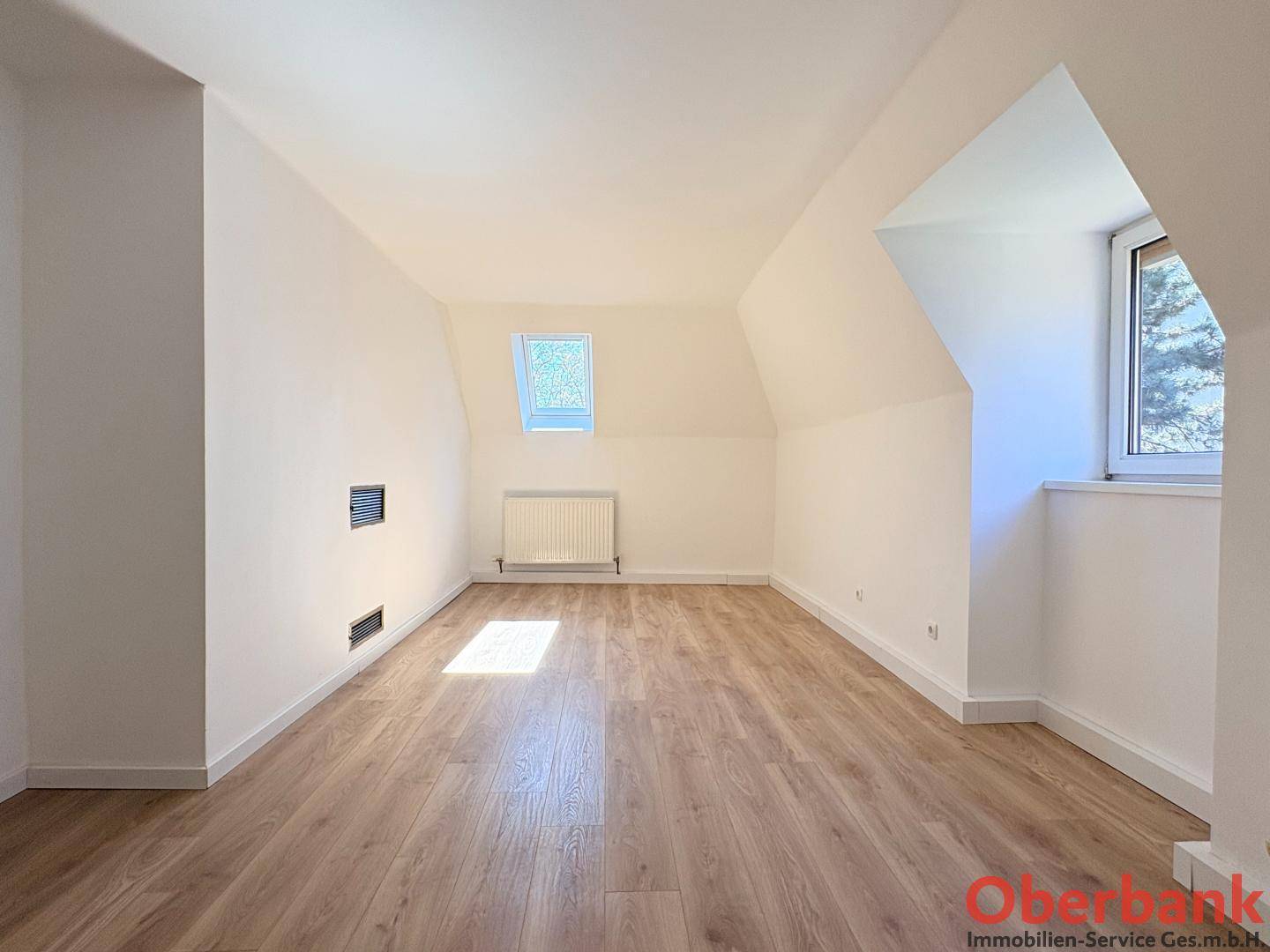 Helles Zimmer im Dachgeschoss mit Holzboden, Dachschrägen und zwei Fenstern für viel Licht.