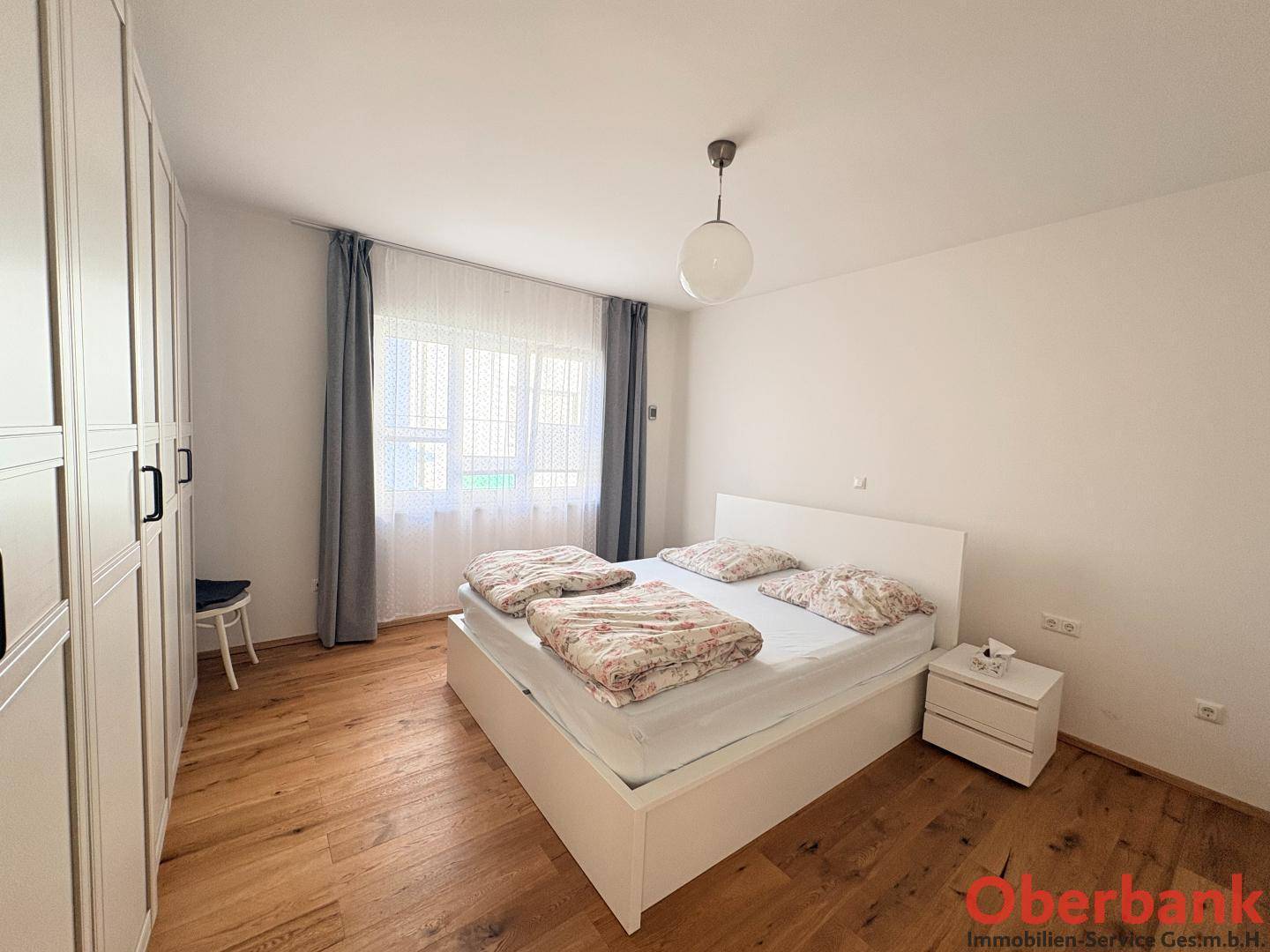 Helles Schlafzimmer mit weißem Bett, großem Kleiderschrank und warmem Holzboden.
