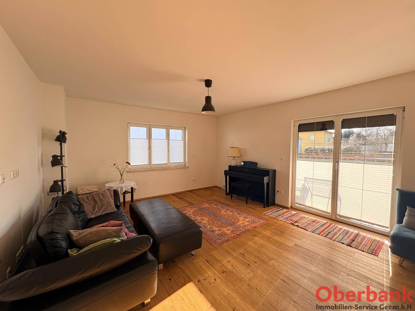 Gemütliches Wohnzimmer mit dunklem Ledersofa, Holzboden und viel Tageslicht durch große Fenster.