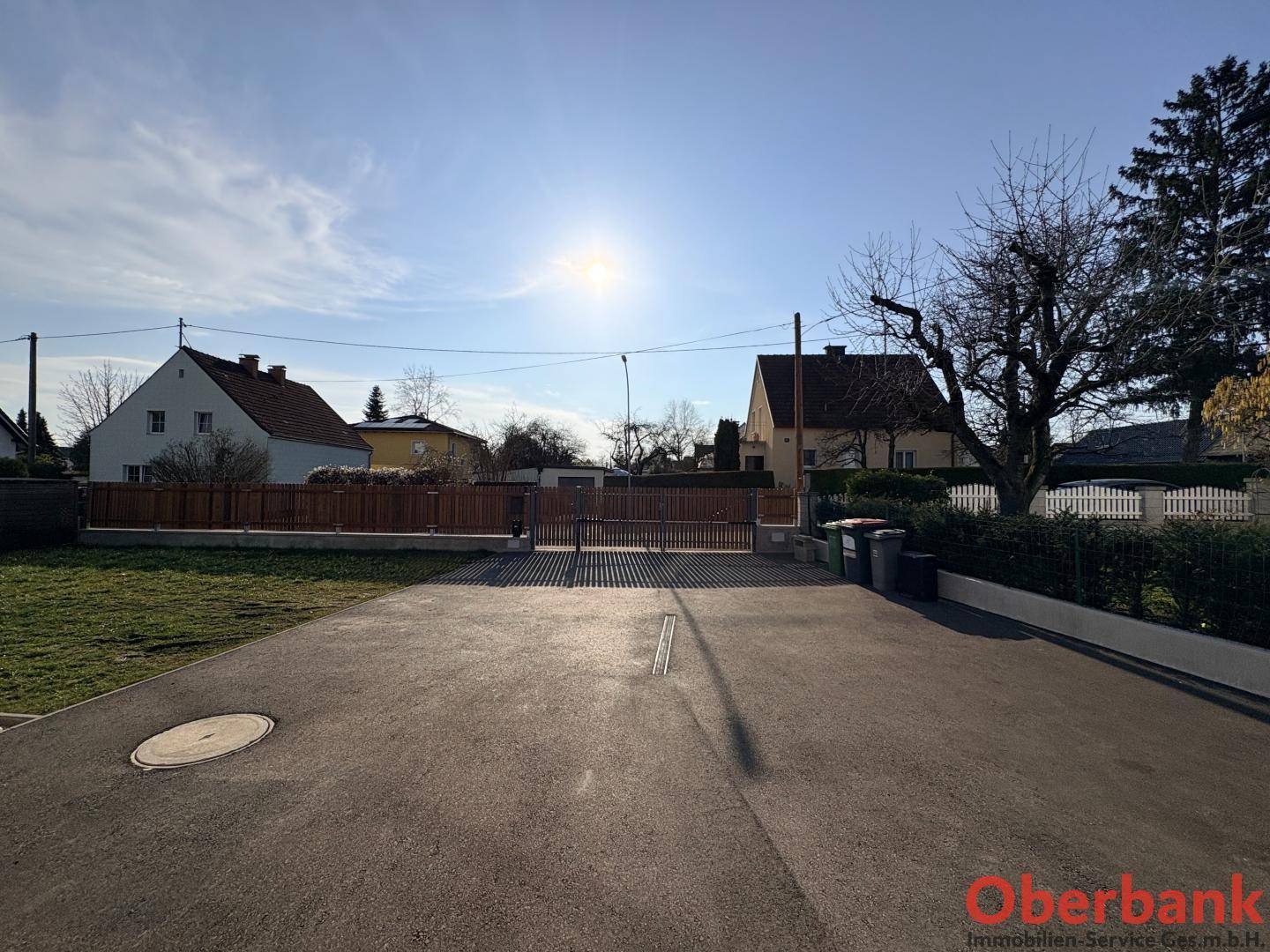Großer gepflasterter Bereich mit Holzzaun und Blick auf die Nachbarschaft unter strahlendem Sonnenschein.