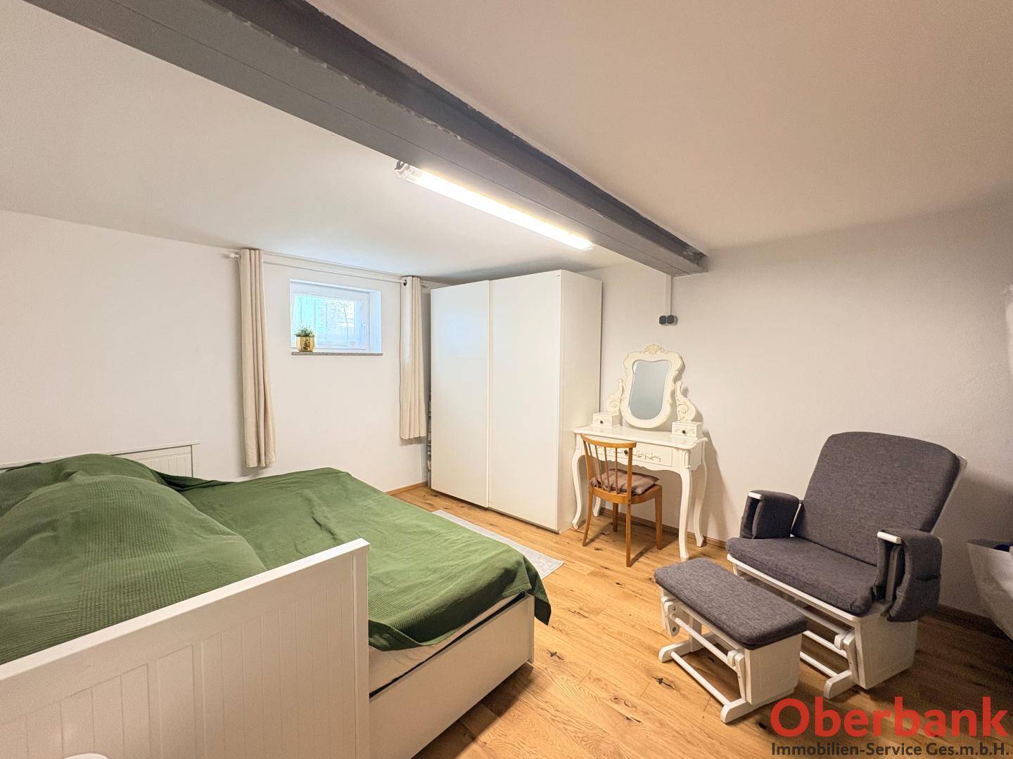 Gemütliches Schlafzimmer mit grünem Bett, weißem Kleiderschrank und Holzboden.