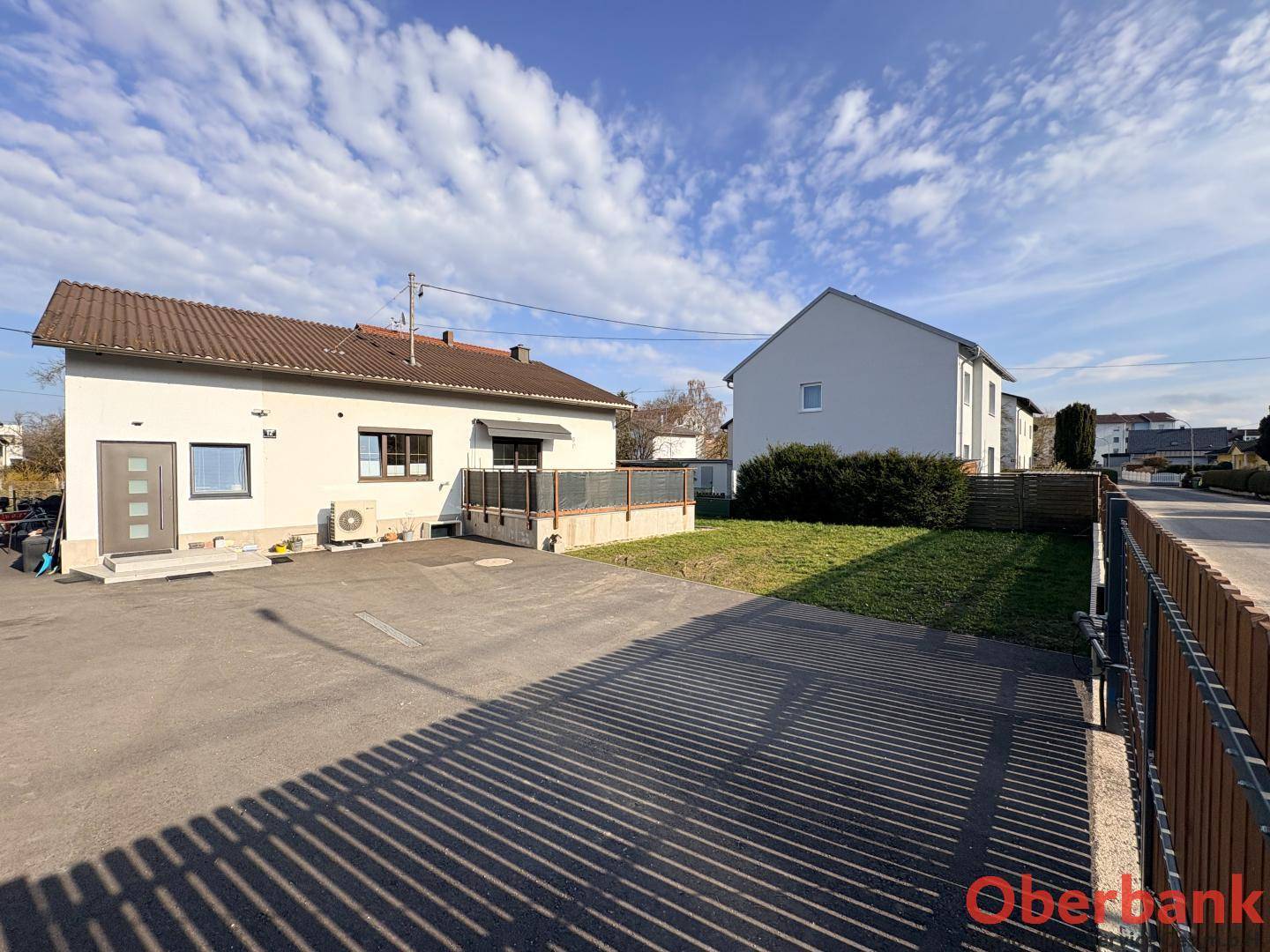 Seitenansicht des weißen Hauses mit großem gepflastertem Bereich und angrenzender Rasenfläche.